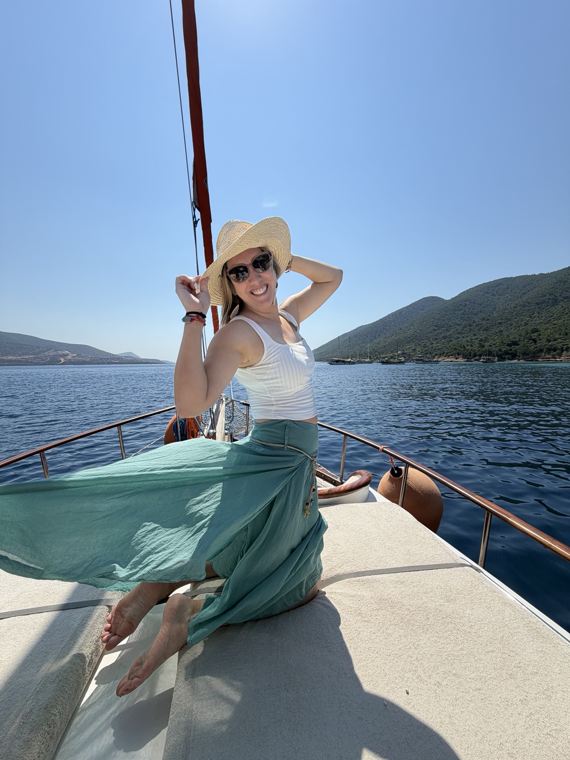 Lindsay smiling on a boat surrounded by blue water and green hills